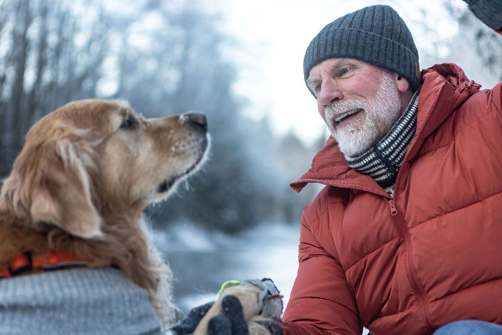 Smilende eldre mann med hund i skogen vinterstid. Demensdugnaden