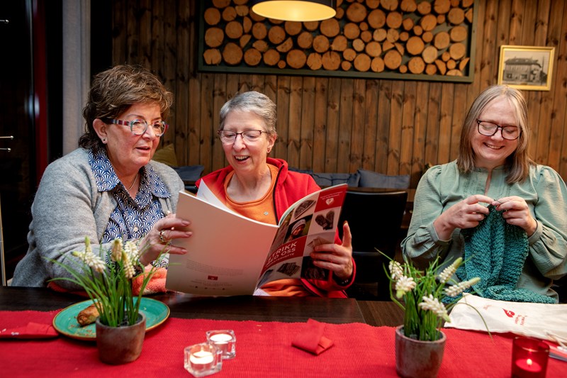 Tre smilende damer som strikker og ser på strikkeoppskrift.