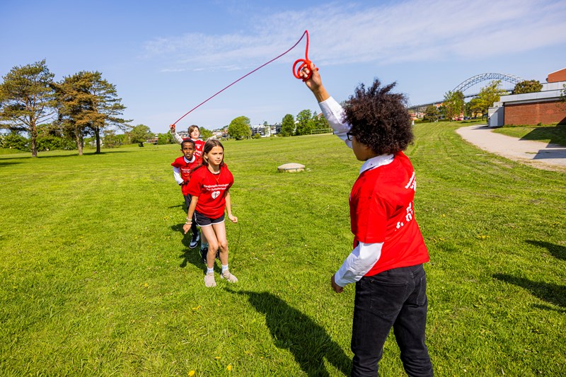 Barn som hopper tau på gresset i vårsolen