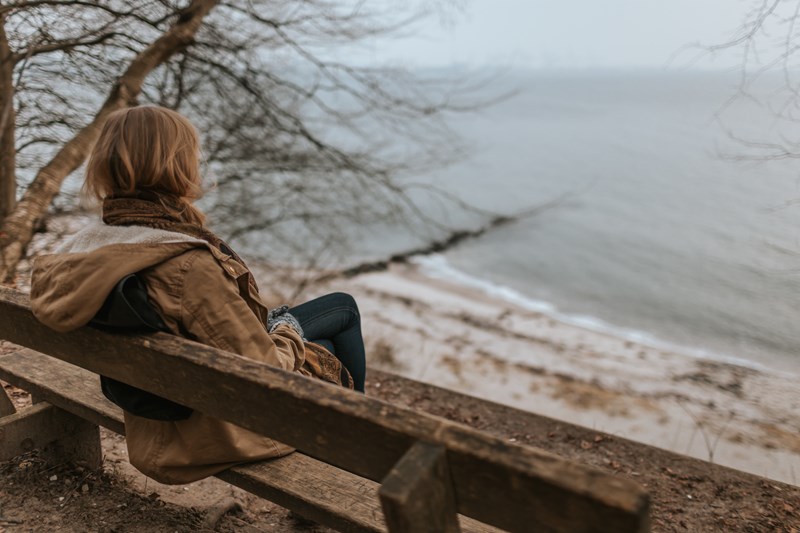 Dame som sitter på benk og ser utover havet. Foto: Krists Luhaers 