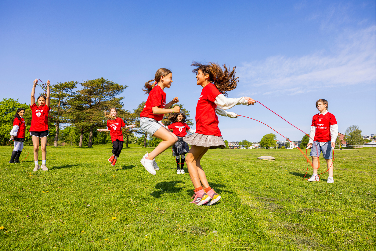 Barn som hopper tau på grønt gress i vårsola